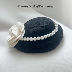 May include: A black lace hat with a white flower and a pearl beaded band. The hat has a rounded crown and a delicate floral lace pattern. The text "Memories Art Treasures" is at the top.