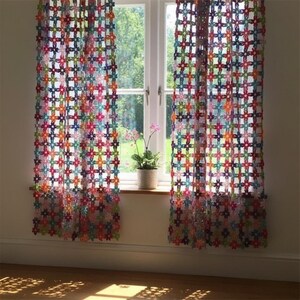 Puede incluir: Cortinas de ganchillo hechas a mano con un colorido estampado floral. Las cortinas están hechas de varios colores, incluyendo rosa, azul, naranja y verde. Cuelgan frente a una ventana con vistas a un jardín verde. Una pequeña planta en maceta está en el alféizar.