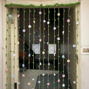 Peut inclure: Un rideau de porte fait à la main au crochet, avec des vignes vertes et de petites fleurs colorées. Le rideau est en fil vert avec une bordure en crochet blanc en haut. Les fleurs sont de couleurs pastel rose, jaune et bleu.