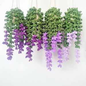 May include: Four handmade crochet hanging plants. Each plant features a green, leafy top and cascading purple and lavender flowers. The plants are suspended by white cords against a white background, creating a charming, handcrafted aesthetic.
