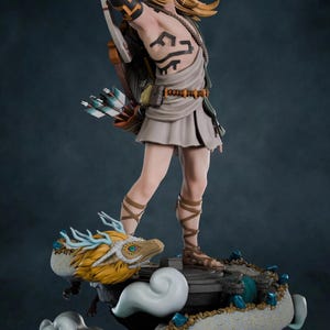 Könnte beinhalten: Detaillierte Figur einer Figur mit blonden Haaren, blauen Augen und einem Tattoo auf dem Arm, die einen Bogen und einen Pfeil hält. Die Figur steht auf einem drachenartigen Wesen mit gelbem und weißem Farbschema. Der Sockel ist dunkelgrau.