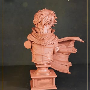 May include: A peach-colored bust of a character with spiky hair, a mask, and a scarf. The figure is on a pedestal with a rectangular base. The bust has a cape draped over its shoulders, and a circular object is attached to the side.