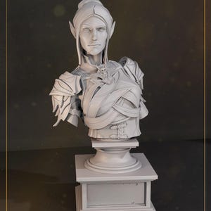 Puede incluir: Busto gris claro detallado de una figura con orejas puntiagudas, que lleva una armadura y un collar decorativo. El busto está montado sobre un pedestal con base cuadrada, mostrando intrincados elementos de diseño. La estética general sugiere un tema de fantasía.