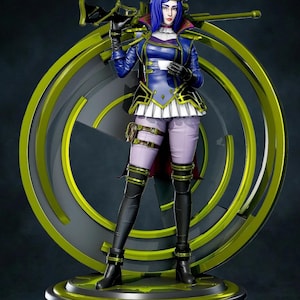 Peut inclure: Figurine détaillée d'une femme en uniforme bleu et blanc de style militaire, tenant une arme. Elle porte un béret blanc, des gants noirs et de hautes bottes noires. La figurine est placée devant un fond de design circulaire stylisé avec des accents jaunes et gris.