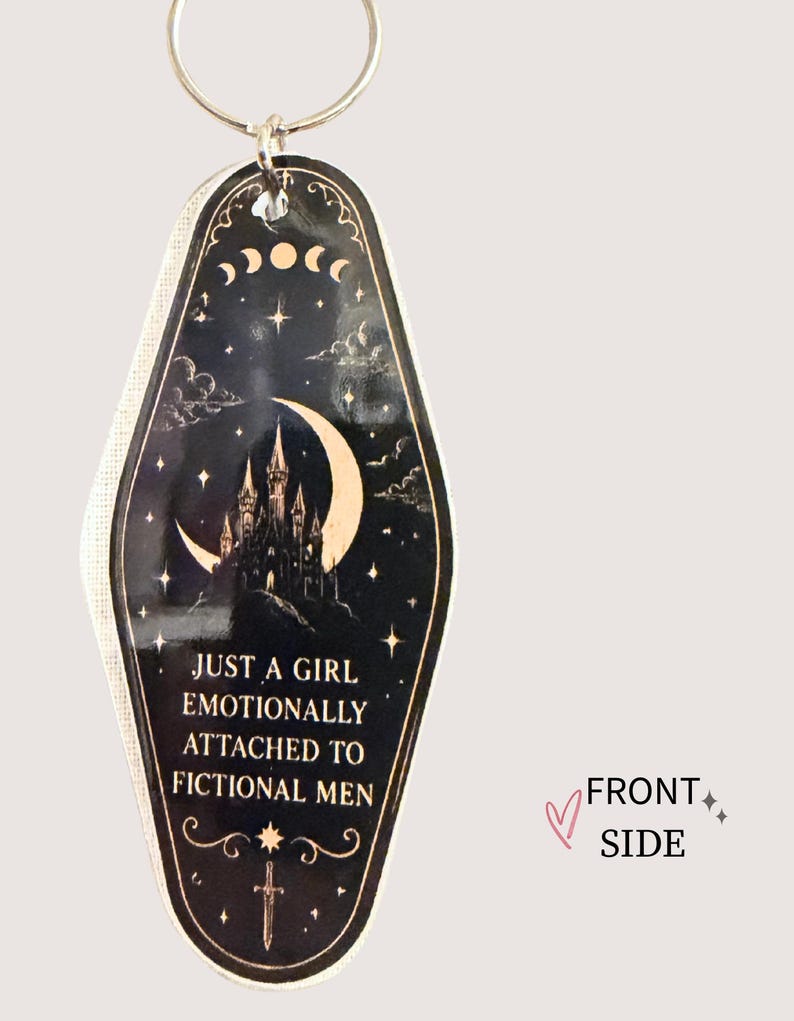 May include: Black and gold keychain with a night sky design, featuring a castle, moon, stars, and the text "JUST A GIRL EMOTIONALLY ATTACHED TO FICTIONAL MEN." The keychain has a silver ring.