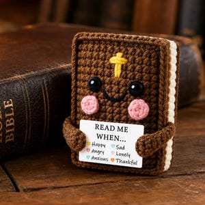May include: A brown crocheted book-shaped plush with a yellow cross, black eyes, and pink cheeks. It holds a white card that reads: READ ME WHEN... Happy, Sad, Angry, Lonely, Anxious, Thankful, each with a small colored heart icon next to it.