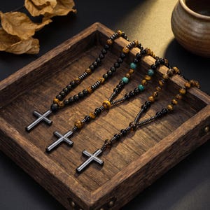 May include: Three beaded necklaces featuring metallic cross pendants. Each necklace is constructed with a combination of black, brown tiger eye, and metallic beads, with one necklace incorporating turquoise-colored beads into the design.