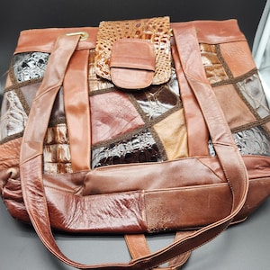 May include: A brown patchwork leather tote bag. The bag has a variety of textures and shades of brown, with a flap closure. The long straps are a darker brown, and the bag shows signs of wear. The bag is a good size for carrying items.