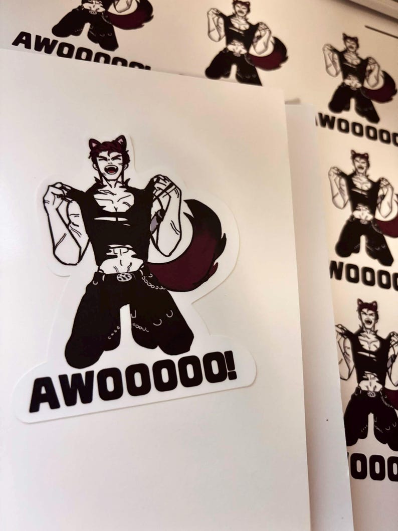 May include: A die-cut sticker featuring a stylised illustration of a character with cat ears, wearing a black sleeveless top and trousers, with a large dark tail. The character is shown in a dynamic pose with the bold black text AWOOOOO! below.
