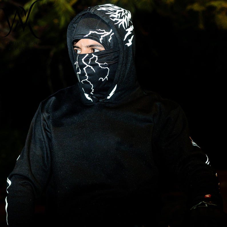May include: A black hooded sweatshirt featuring a white lightning bolt pattern on the hood and a matching black face mask with a white lightning bolt design. The garment includes long sleeves with white lightning accents along the outer arms.