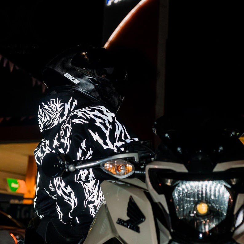 May include: A black hoodie featuring a white, jagged, flame-like graphic pattern across the fabric. The hoodie is worn with a black carbon-fiber style motorcycle helmet with the text SKB visible on the side, positioned on a white motorcycle.