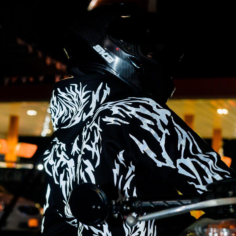 May include: A black hooded sweatshirt featuring a white, jagged, lightning-like graphic pattern across the back and hood. The garment is worn with a black motorcycle helmet that displays the white text SKA on the side of the shell.