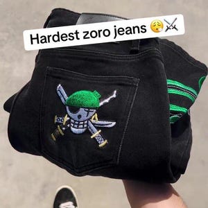 May include: Black denim jeans with a green and white embroidered design on the back pocket. The jeans feature the text "Hardest zoro jeans" and a logo. The Washington Apperal logo is visible in the upper left corner.
