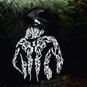 May include: A black hooded sweatshirt featuring a reflective white tribal-style graphic pattern across the back and hood, worn with a black motorcycle helmet. The design consists of sharp, jagged lines that contrast against the dark fabric.