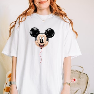 Könnte beinhalten: Weißes T-Shirt mit einem Mickey Mouse Ballon-Design. Der Ballon hat schwarze Ohren, ein lächelndes Gesicht und eine rote Schnur. Das Shirt ist ein lockerer, übergroßer Stil.