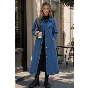 Peut inclure: Un long manteau en jean bleu arrivant jusqu'aux pieds, doté de manches longues, d'un col classique, d'une fermeture boutonnée sur toute la longueur avec des boutons argentés, de deux poches poitrine à rabat et d'un ourlet droit, porté sur un col roulé noir.