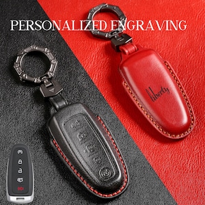 Peut inclure: Deux étuis de porte-clés en cuir, un noir et un rouge, avec des porte-clés en métal. Le couvercle noir a des coutures rouges et le couvercle rouge porte le mot "liberty". Le texte "PERSONNALISÉ GRAVURE" est en haut.