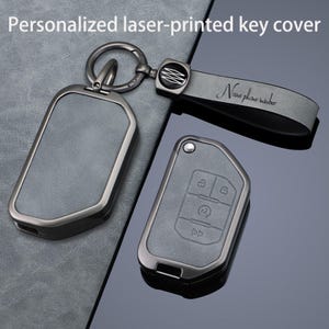 May include: A set of personalized laser-printed key covers. The covers are gray with a metallic frame and a keychain. One cover has a strap with the text "Name phone number". The other cover has key symbols.