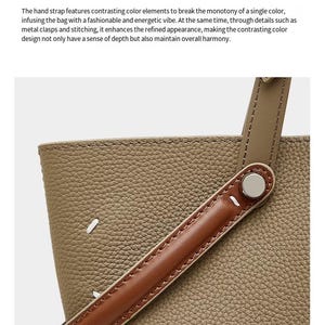 May include: A close-up of a handbag. The bag has an olive-green textured body and a brown leather handle. The handle is attached with a silver metal clasp. The text "Striped design for the hand strap" is at the top.