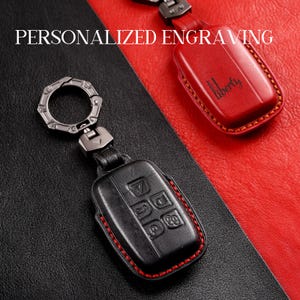 May include: Black leather key fob with red stitching and silver hardware. The fob has embossed buttons and is attached to a key ring. A red leather key fob with the word "Liberty" is also shown. The text "PERSONALIZED ENGRAVING" is at the top.