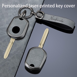 May include: A set of personalized laser-printed key covers. The keys are gray with a silver key ring and a gray leather strap. The strap has the text "Name phone number" printed on it. The key covers have a black circle and the key has a silver blade.