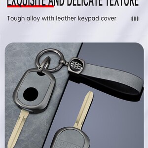 May include: A set of car keys with a zinc alloy key fob and a leather strap. The key fob is dark gray with a black button and a silver key ring. The text "ZINC ALLOY MATERIAL EXQUISITE AND DELICATE TEXTURE" is visible.