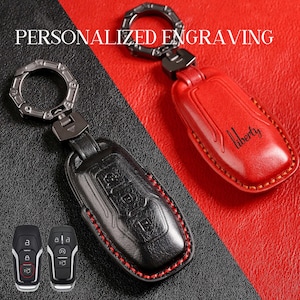 Puede incluir: Fundas de cuero para llaveros, una negra y otra roja, con llaveros de metal. La funda negra tiene costuras rojas, y la roja tiene la palabra "Liberty". La imagen también muestra dos mandos de coche y el texto "PERSONALIZED ENGRAVING".