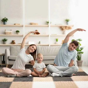 May include: A family of three doing yoga together indoors. The mother and father are stretching their arms up and to the side, while the baby sits between them. They are all wearing casual clothing and are on a patterned rug.