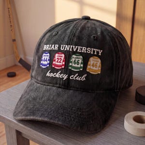 May include: Black baseball cap with the text "Briar University hockey club." The cap features embroidered jersey patches with player names and numbers. A hockey stick and puck are visible in the background.