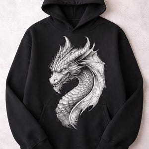 May include: Black hooded sweatshirt featuring a detailed grayscale illustration of a dragon's head and neck. The dragon has textured scales, horns, and a wing. The design is centered on the front of the hoodie.