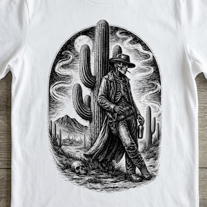 May include: White t-shirt with a black and white illustration of a skeleton cowboy leaning against a cactus. The design includes a desert landscape, a skull, and a smoking skeleton.