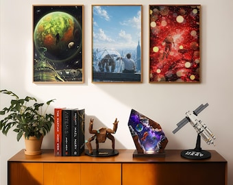 Könnte beinhalten: Drei gerahmte Poster mit Weltraummotiven hängen über einem Holzschrank mit einer Topfpflanze, drei Büchern, einer braunen geometrischen Kreaturenfigur, einer leuchtenden Harzlampe mit Astronautenszene und einem weiß-schwarzen Satellitenmodell.
