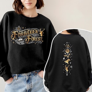 Può includere: Felpa nera con testo e grafica dorati "Forbidden Forest National Park" sul davanti. Il retro presenta grafiche dorate tra cui un cervo, un cappello e un boccino d'oro. La felpa è girocollo.