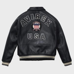 Men’s black leather bomber jacket with front zip closure, ribbed cuffs, striped hem, and USA shield chest patch.