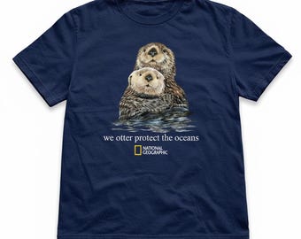May include: Navy blue t-shirt featuring a detailed illustration of two sea otters in water. The shirt includes the text "we otter protect the oceans" and the National Geographic logo. A casual, short-sleeved tee.