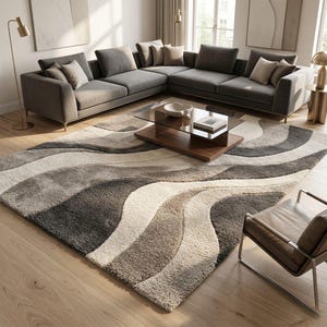 Könnte beinhalten: Ein modernes Wohnzimmer mit einem großen grauen Ecksofa und beigen Kissen. Ein gemusterter Teppich in Grau-, Beige- und Weißtönen bedeckt den Boden. Ein Couchtisch mit Glasplatte und ein Ledersessel vervollständigen die Szene.