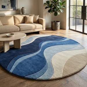 May include: A circular rug with a flowing, wave-like pattern in shades of blue and beige. The rug's design incorporates dark navy, light blue, and beige hues, creating an ocean-inspired aesthetic. It is placed on a wooden floor.