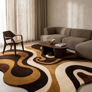 May include: A large, irregularly shaped area rug featuring a flowing, abstract pattern of wavy, interlocking bands in shades of dark brown, medium tan, and cream. The rug has a thick, plush texture and covers a significant portion of the floor area.