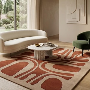 Könnte beinhalten: Ein rechteckiger Teppich mit einem großflächigen abstrakten Muster in Terrakotta-Orange und Beige. Das Design besteht aus geschwungenen, bogenartigen Formen und abgerundeten Blöcken, die einen kräftigen grafischen Kontrast auf dem Boden bilden.