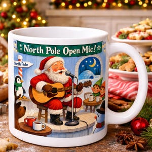 May include: A white ceramic mug featuring a colorful illustration of Santa Claus playing an acoustic guitar on a stage. The text North Pole Open Mic is printed at the top. The scene includes a penguin, a reindeer, and elves in the background.