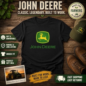 Puede incluir: Camiseta negra con el logo de John Deere, un emblema de ciervo verde y amarillo, y el nombre de la marca en verde. La imagen incluye una gorra verde, botas marrones y el texto "Built for Work. Made to Last."