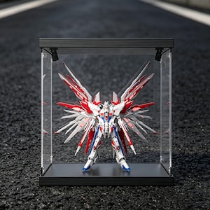 May include: A detailed model robot with red, white, blue, and silver accents is displayed inside a clear acrylic case with a black frame. The robot has large, wing-like structures extending from its back.