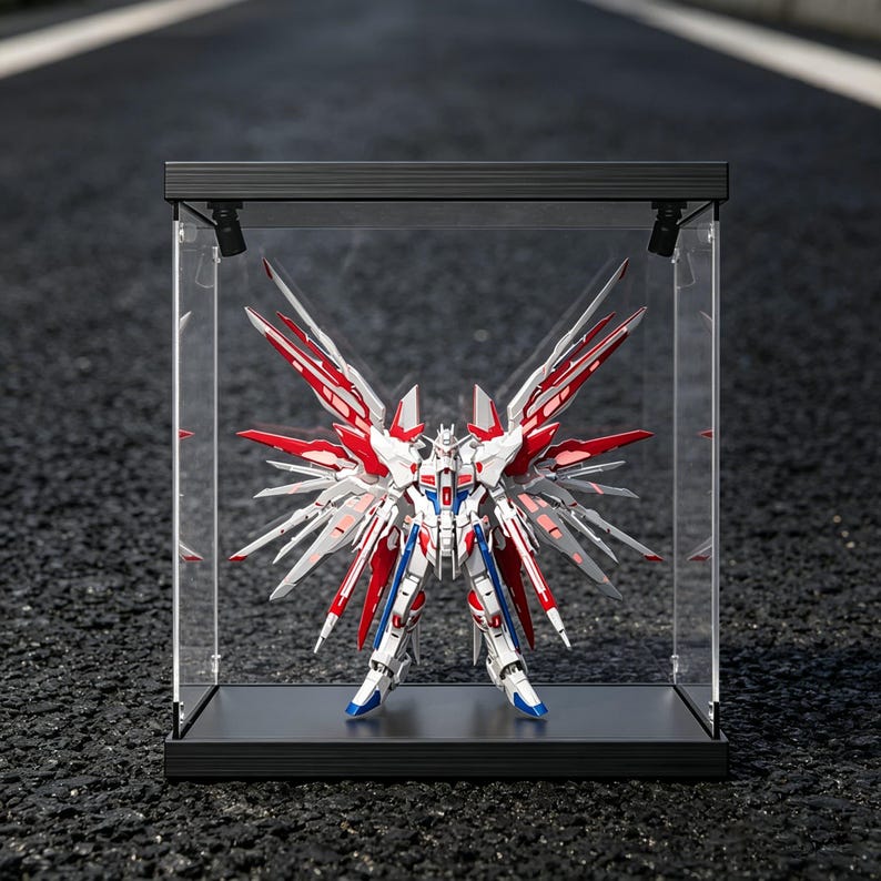 May include: A detailed model robot with red, white, blue, and silver accents is displayed inside a clear acrylic case with a black frame. The robot has large, wing-like structures extending from its back.