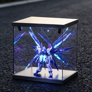 May include: A detailed model of a robot, primarily white and blue, is displayed inside a clear, illuminated display case. The robot has large, stylized wings and is lit with blue and white lights. The display case has a metallic frame.
