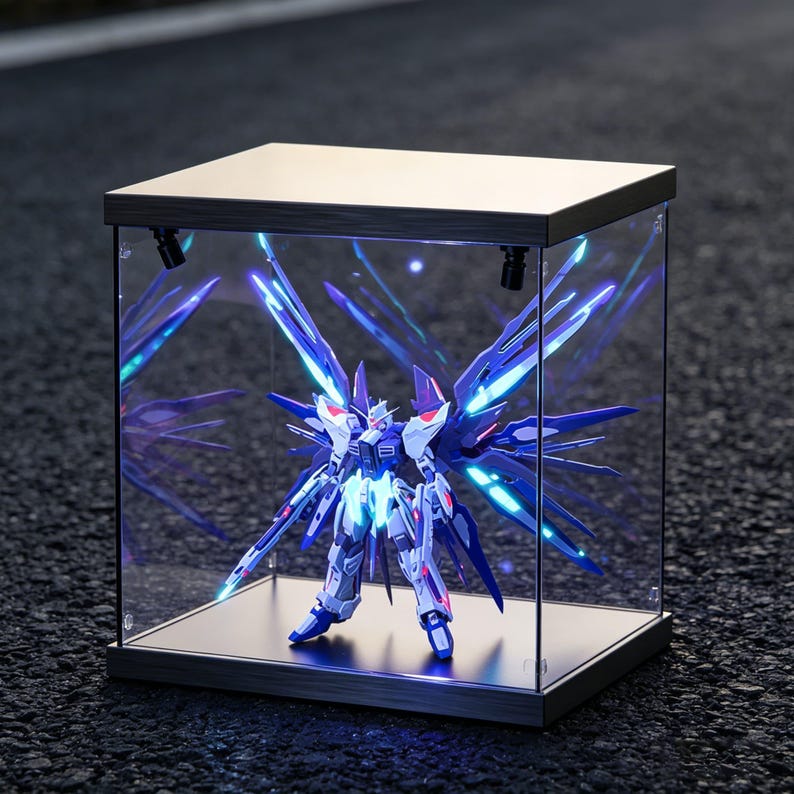 May include: A detailed model of a robot, primarily white and blue, is displayed inside a clear, illuminated display case. The robot has large, stylized wings and is lit with blue and white lights. The display case has a metallic frame.