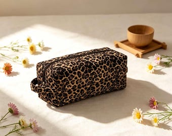 May include: A rectangular quilted pouch featuring a black and tan leopard print pattern. The pouch has a black zipper closure along the top and a small fabric handle on the side. The exterior fabric has a stitched diamond pattern throughout.