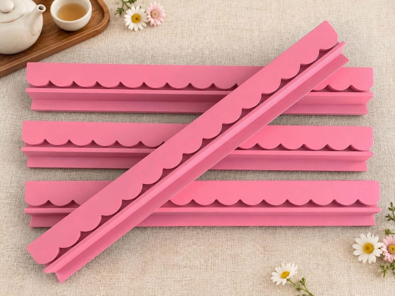 May include: Four long, pink, L-shaped shelf strips featuring a decorative scalloped edge along the top. The strips are arranged with three lying horizontally and one placed diagonally across them, showcasing the uniform matte finish.