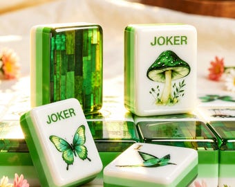 Puede incluir: Un conjunto de fichas de mahjong rectangulares con diseños en verde y blanco. Algunas fichas muestran una mariposa verde, un hongo verde con el texto JOKER o un pájaro verde. Otras fichas tienen un patrón de mosaico verde translúcido en el reverso.