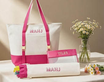 May include: A white and hot pink canvas tote bag with the text MAHJ, a matching cylindrical case with the text MAHJ, and a rectangular clear pouch with hot pink trim and the text TILES. The set features gold-toned hardware and pink straps.