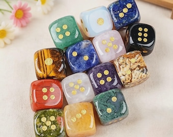 May include: A collection of thirteen multi-colored dice crafted from various polished stones and minerals. Each die features smooth, rounded edges and gold-colored circular pips inlaid on the faces to indicate numerical values from one to six.